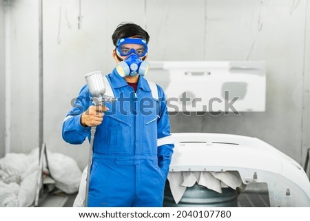 Mechanic Asian man spray painting airbrush pulverizer car body in paint chamber repairing car automobile vehicle parts using tools equipment in workshop garage support service in overall work uniform