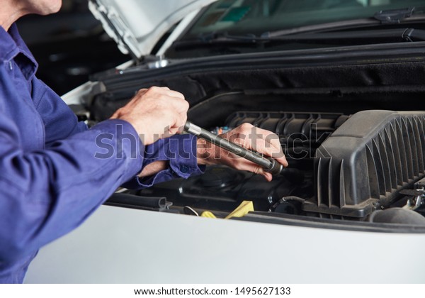 Mechanic at auto inspection or tuning screws with\
tool on engine