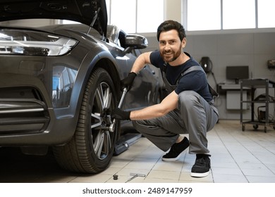 Mechanic in auto repair shop working on car wheel, using wrench. Professional mechanic delivering car maintenance service with smile. Modern workshop environment with car repair tools. - Powered by Shutterstock