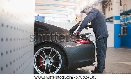Mechanic in automobile garage checking hood for the luxury car, close up