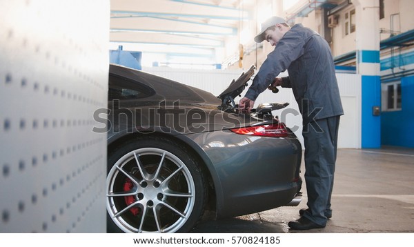 Mechanic in automobile garage checking hood for the\
luxury car, close up