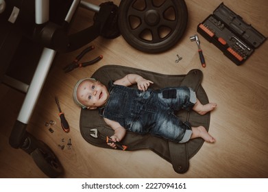 Mechanic baby boy repairing his baby stroller. Humor. Kid with tools changes the wheel. Top view. - Shutterstock ID 2227094161
