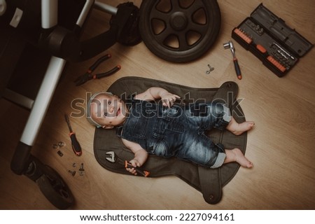 Mechanic baby boy repairing his baby stroller. Humor. Kid with tools changes the wheel. Top view.