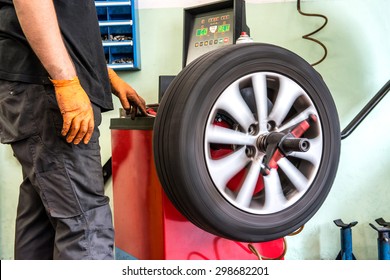 Mechanic Balancing A Car Wheel On An Automated Machine Checking The Readout On The Digital Display Before Adding The Weights