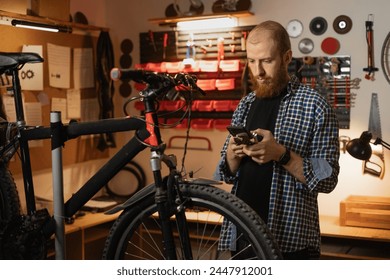 Mechanic in a bicycle repair workshop using smartphone reading a message or searching information online about bike. Copy space - Powered by Shutterstock