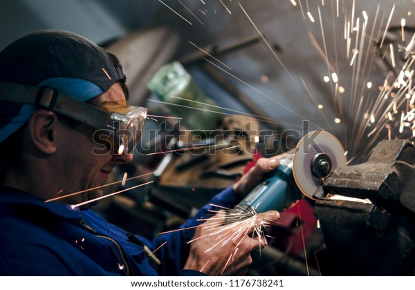mechanic\
in blue uniform, cuts the steel part with an angle grinder in the\
garage. In workshop. the concept of protection technology in the\
workplace, eye protection. sparks fly in the\
eye