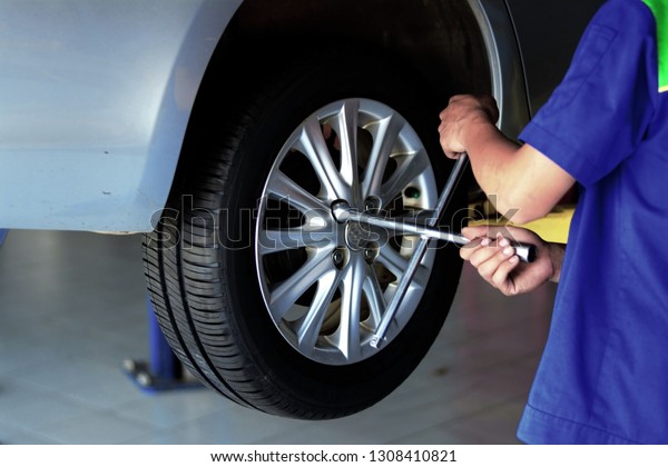 the mechanic in blue uniform using cross wrench\
tighten the bolts wheel
