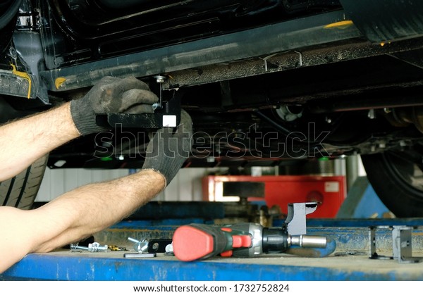 A mechanic in a car repair\
shop installs holders for installing thresholds on a passenger\
car.