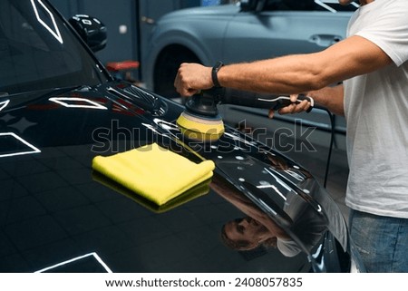 Mechanic in car repair shop polishes the hood of black car
