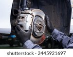 a mechanic at a car service diagnoses and replaces the caliper and brake pads in the front of the car. Car without wheels. metal spare parts. holds the brake disc with both hands