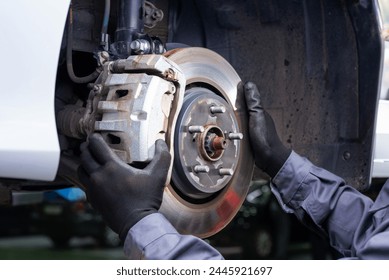 a mechanic at a car service diagnoses and replaces the caliper and brake pads in the front of the car. Car without wheels. metal spare parts. holds the brake disc with both hands - Powered by Shutterstock