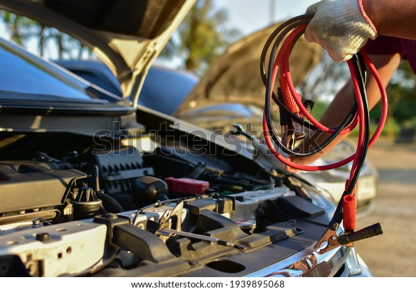 A mechanic carries a car battery charger to charge\
electricity through a jumper cable to another car on a country\
road.