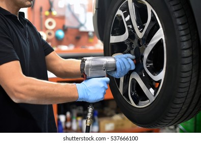 Mechanic Changing A Car Tire In A Workshop On A Vehicle On A Hoist Using An Electric Drill To Loosen The Bolts In A Concept Of Service Or Replacement