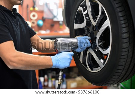 Mechanic changing a car tire in a workshop on a vehicle on a hoist using an electric drill to loosen the bolts in a concept of service or replacement