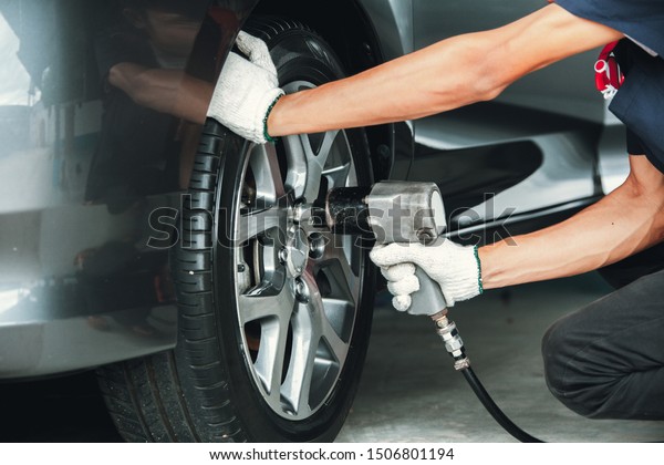Mechanic changing wheel on car\
with impact wrench. mechanic man with electric screwdriver changing\
tire outside. Car service. Hands replace tires on\
wheels.