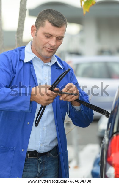 mechanic\
changing windshield wiper blades on a\
car