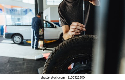 Mechanic checking car tire tread depth with caliber. Technician examining the car tire grip with a measuring instrument in service station.