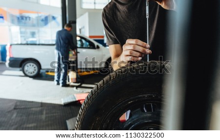 Mechanic checking car tire tread depth with caliber. Technician examining the car tire grip with a measuring instrument in service station.