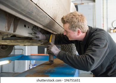 A Mechanic Is Checking The Chassis Number From A Lifted Car On A Bridge In A Garage.