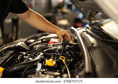 Mechanic checking engine oil level by pulling out the dipstick. Routine car maintenance in a professional auto workshop.