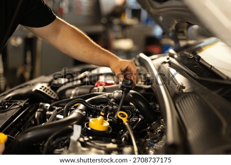 Mechanic checking engine oil level by pulling out the dipstick. Routine car maintenance in a professional auto workshop.