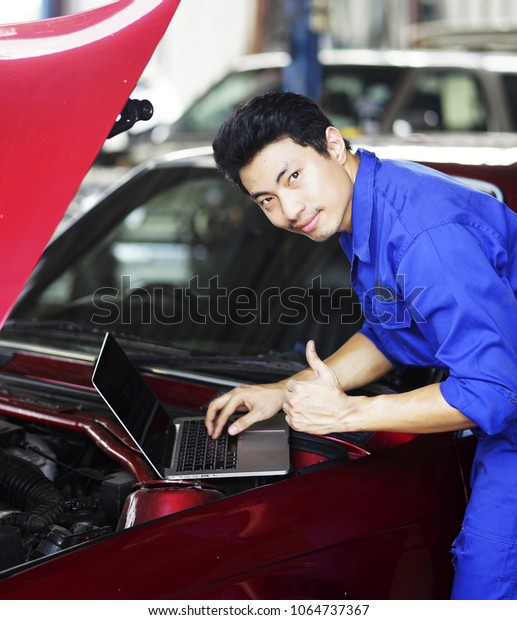 Mechanic checking and fix car within\
garage. Mechanic in auto repair shop standing next to car with open\
hood. Young man open car hood and set up engine.\
