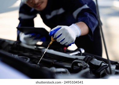 A mechanic is checking the oil in a car. The oil is low and the mechanic is adding more - Powered by Shutterstock