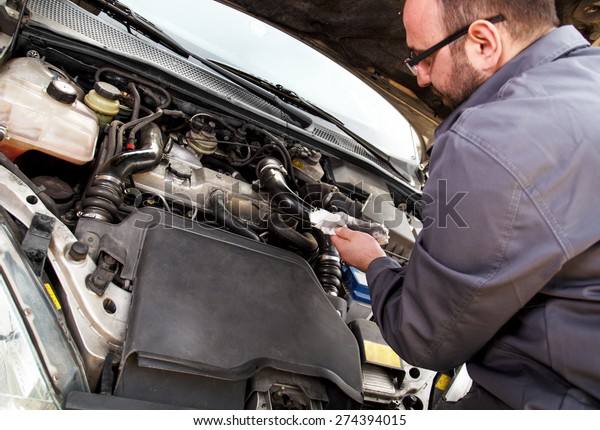A\
mechanic checks the oil on a car being\
repaired