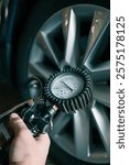 A mechanic checks tire pressure with a gauge during routine car maintenance in a garage. Focus on the wheel and the instrument ensuring optimal vehicle safety and performance.