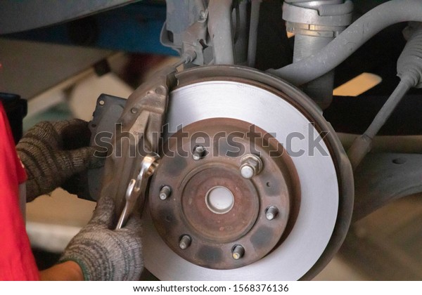 The mechanic is cleaning the\
front wheel brake set of the car before changing to a new wheel ,He\
wears cloth gloves. Hold the wrench and brake pads in the\
hand.