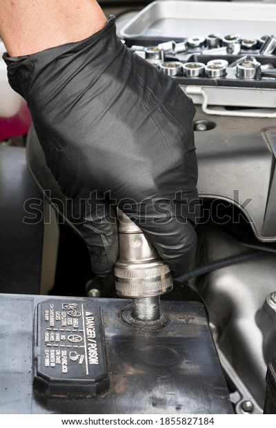 A mechanic\
cleans a battery terminal with a wire battery terminal brush during\
routine automobile maintenance.\

