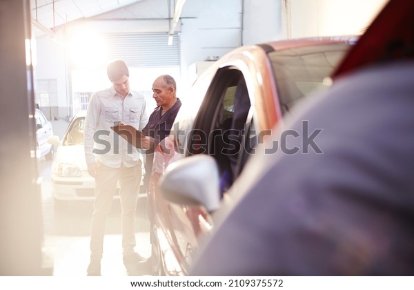 Mechanic with clipboard talking to customer in auto\
repair shop