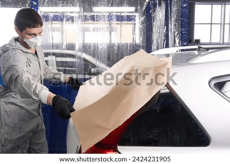 Mechanic covering car with paper before painting in auto repair service