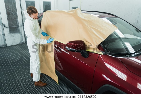 Mechanic covering car with paper and tape\
before painting in auto repair service\
booth