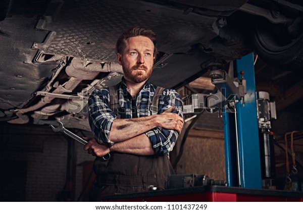 Mechanic crossed hands while standing under
lifting car in a repair
garage.