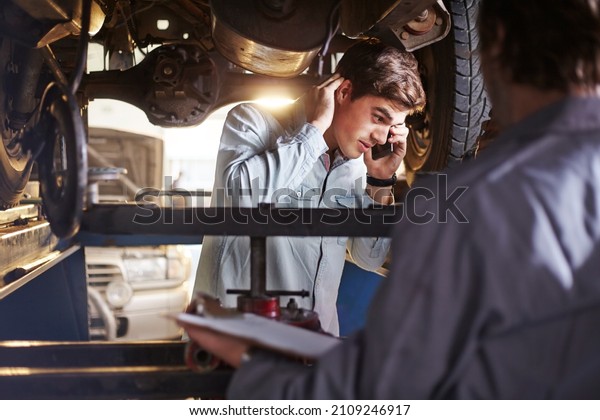 Mechanic and\
customer talking on cell phone under\
car