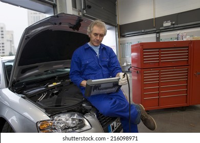 Mechanic With Diagnostic Computer On Car With Open Bonnet