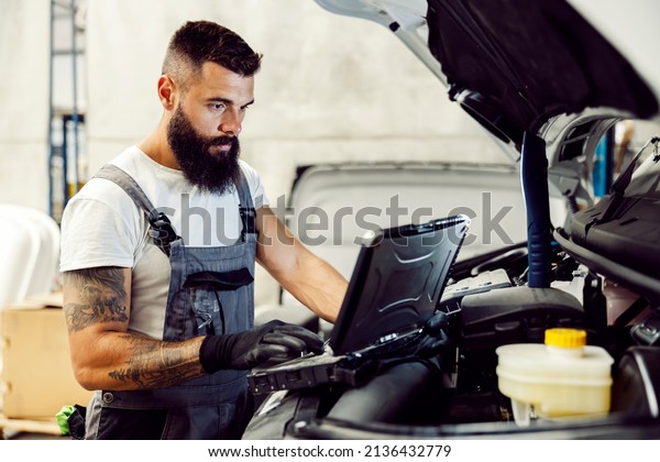 A mechanic diagnostic a problem with auto on\
laptop at workshop.