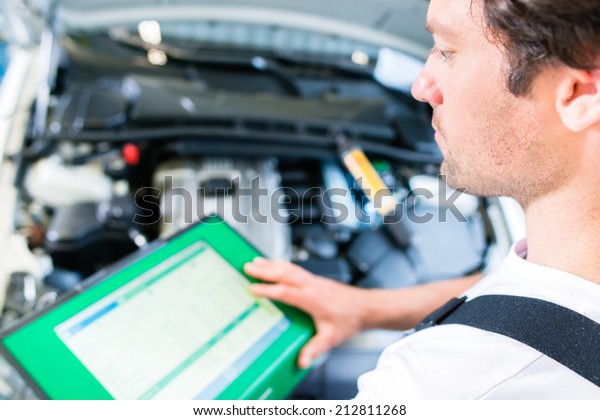 Mechanic with\
diagnostic tool in car\
workshop