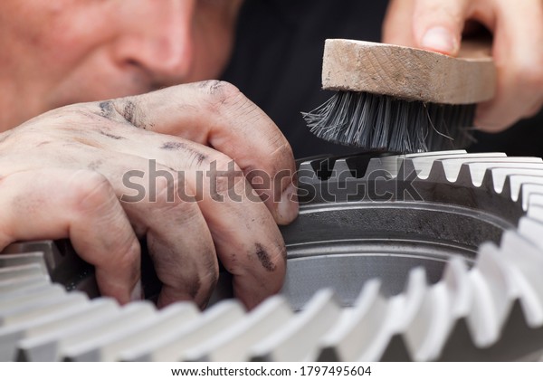 Mechanic with dirty hands cleaning a\
cog wheel with a steel brush- selective focus on the\
hand