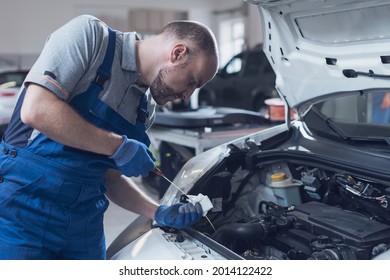 Mechanic doing a vehicle inspection, he is checking a car's oil level and quality using a dipstick
