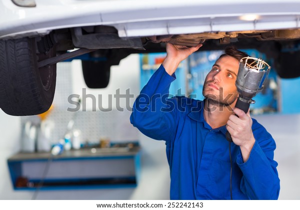 Mechanic examining under the car with torch at the\
repair garage