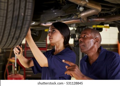 Mechanic And Female Trainee Working Underneath Car Together