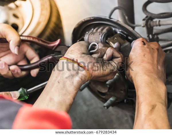 Mechanic fixing rear brake pad of the drum brake\
with the assist of second mechanic at tire maintenance service\
shop. Selective focus.