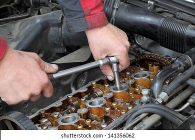 Mechanic fixing spark plug to open car engine with ratchet, visible camshafts,  pulley, belt, timing chain