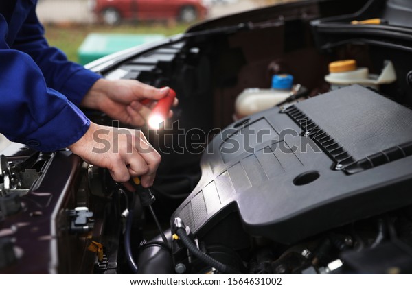 Mechanic\
with flashlight fixing car outdoors,\
closeup