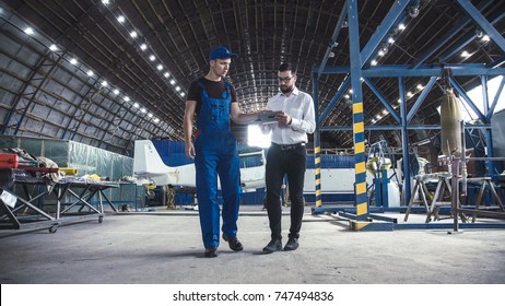 Mechanic and flight engineer having a discussion together as they stand in aircraft in a hangar. - Powered by Shutterstock