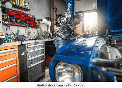 Mechanic is focused on repairing a classic blue car in a well-organized garage workshop. Tools and equipment surround him as he assesses the vehicle's condition, ensuring a meticulous restoration proc - Powered by Shutterstock