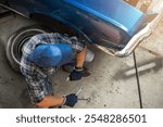 A mechanic focuses on repairing a classic car in a garage, surrounded by tools and an old tire, emphasizing dedication to the craft.