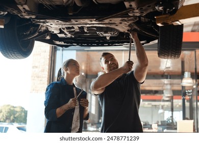 Mechanic, garage and tools for car with training, maintenance engineer and teamwork at workplace. Repair shop, trade and mentor with woman checking under wheel with technician and auto service - Powered by Shutterstock